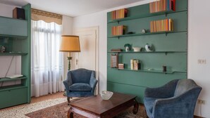 Un soggiorno con una libreria verde, due poltrone blu, un tavolino in legno e una lampada.
