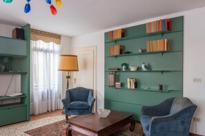 A living room with a green bookshelf, two blue armchairs, a wooden coffee table, and a lamp. - Ca' Magno, an enchanting place in Venice (Venezia)