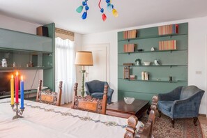 A room with a bed, two armchairs, a table, a bookshelf, and a chandelier.