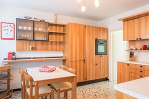 A compact kitchen with wooden cabinets, a built-in oven, and a dining area with a table and chairs. - Ca' Magno, an enchanting place in Venice (Venezia)