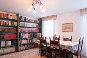 A library with wooden bookshelves filled with books, a dining table with chairs, and a chandelier.