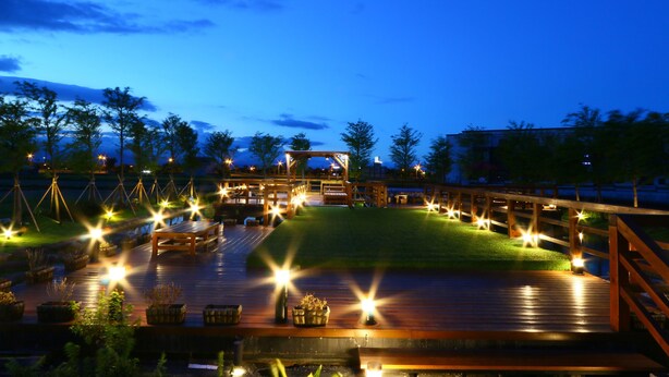 A wooden deck with outdoor seating and string lights, surrounded by trees and a grassy area. - Luoyuxuan (Wujie)