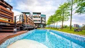 A swimming pool with a tiled edge, surrounded by a wooden deck and a building with multiple floors and balconies. - Luoyuxuan (Wujie)