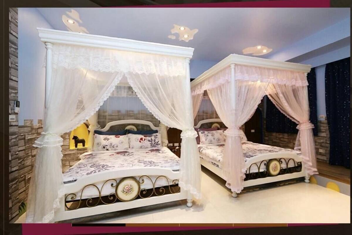 Two four-poster beds with white canopies, a stone wall, and a night sky view.