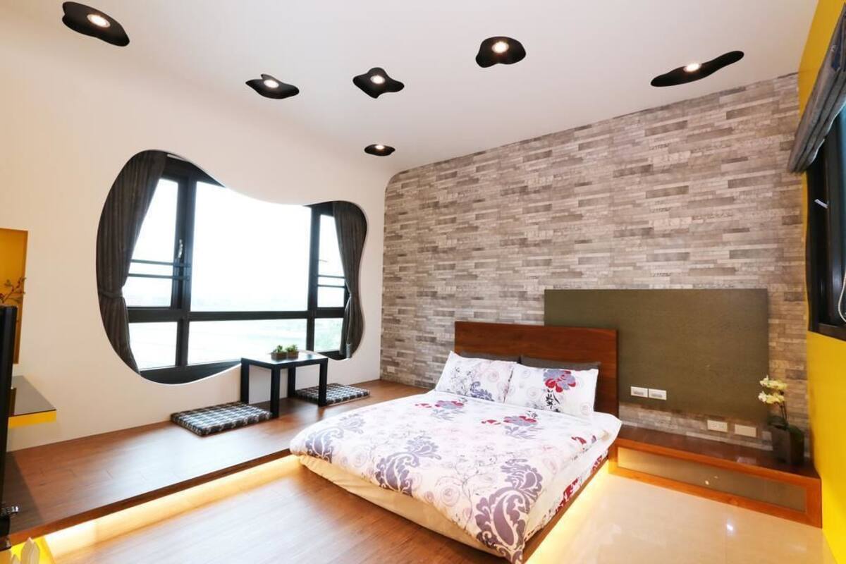 A modern bedroom with a large bed, a brick-patterned wall, and recessed ceiling lights.