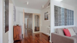 Un salon moderne avec un parquet, un canapé gris agrémenté de coussins rouges, un meuble en bois et un grand tableau abstrait accroché au mur.