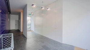 Un couloir moderne avec un mur blanc incurvé, un sol carrelé gris et des luminaires suspendus.