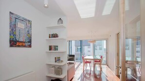 Un appartement moderne avec un plancher en bois, un coin repas avec des chaises rouges, une bibliothèque et une grande fenêtre donnant sur la ville.