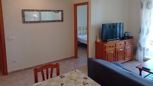 Un soggiorno con TV, mobiletto in legno e zona pranzo con tavolo e sedie.