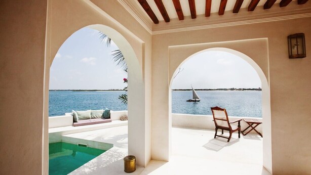 A pool area with a view of the sea, a sailboat, and a wooden chair. - Luxury beachfront holiday house, pool garden all sea views, Forodhani House Lamu (Lamu)