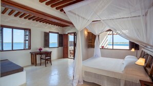 A bedroom with a bed, a desk, and a chair, large windows with shutters, and a view of the sea. - Luxury beachfront holiday house, pool garden all sea views, Forodhani House Lamu (Lamu)