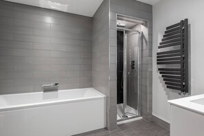 Un baño moderno con ducha de vidrio, una bañera blanca y un perchero de toallas en la pared.