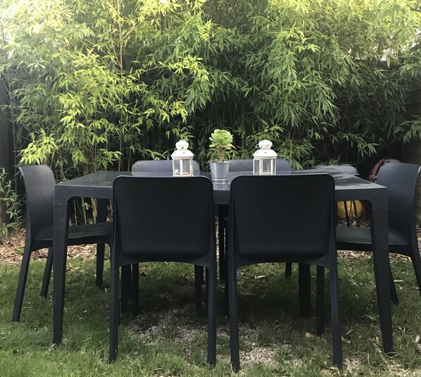 A black table set outdoors with chairs, surrounded by a bamboo fence and greenery.
