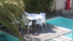 Un área de piscina con una mesa redonda y cuatro sillas, rodeada por una terraza de madera.