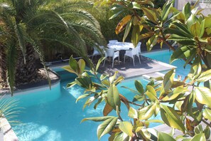 A pool area with a table and chairs, surrounded by palm trees and other greenery. - Very beautiful villa, superb swimming pool, close to the sea, ideal family 5/6 pers (Pérols)