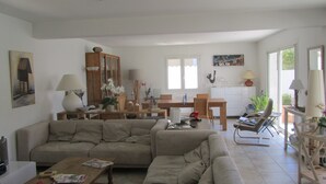 Amplia sala de estar con un sofá grande, una mesa de centro de madera y una mesa de comedor. Se observa un aparador con puertas de vidrio y un cuadro en la pared.