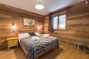 Una habitación con paneles de madera, una cama, mesitas de noche, un cuadro y una ventana.