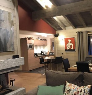 Una sala de estar acogedora con chimenea, un comedor con mesa y sillas, y una cocina al fondo.