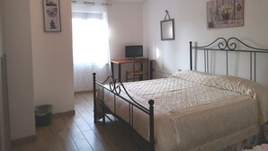 Ein Schlafzimmer mit einem Bett, einem Schreibtisch, einem Stuhl, einem Fernseher und einer kleinen Mülltonne.