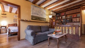 Een gezellige woonkamer met een grijze bank, houten boekenkasten en een eettafel met een fruitschaal.
