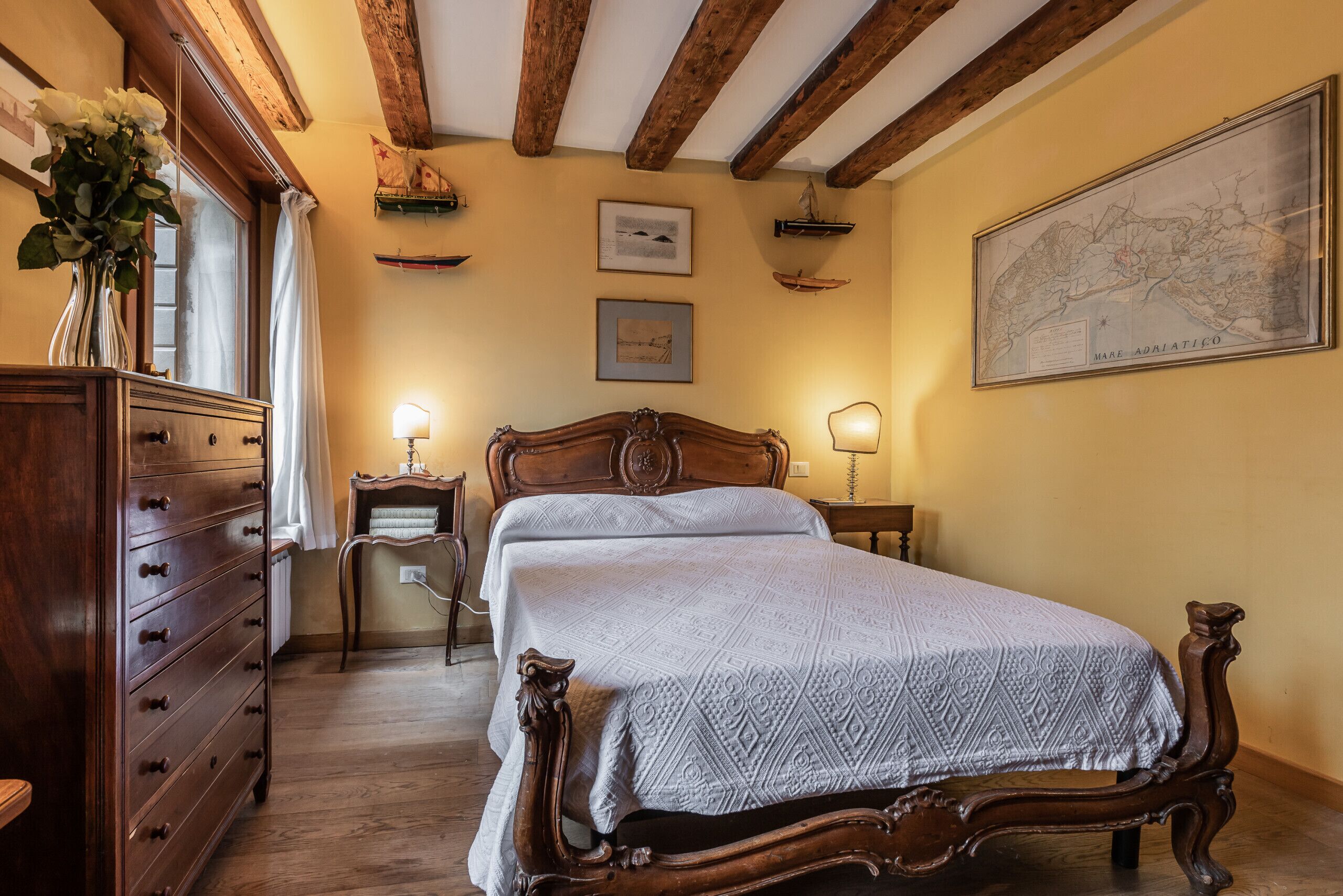 A bedroom with a wooden bed, a dresser, a nightstand, and a map on the wall.