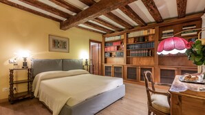 Een slaapkamer met een bed, houten boekenplanken, een bureau met een lamp en een houten stoel.