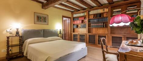A bedroom with a bed, wooden bookshelves, a desk with a lamp, and a wooden chair.