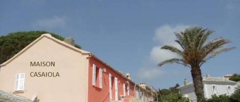 Un edificio con fachada roja, identificado con el nombre 'MAISON CASAIOLA', una escalera y una palmera en primer plano.