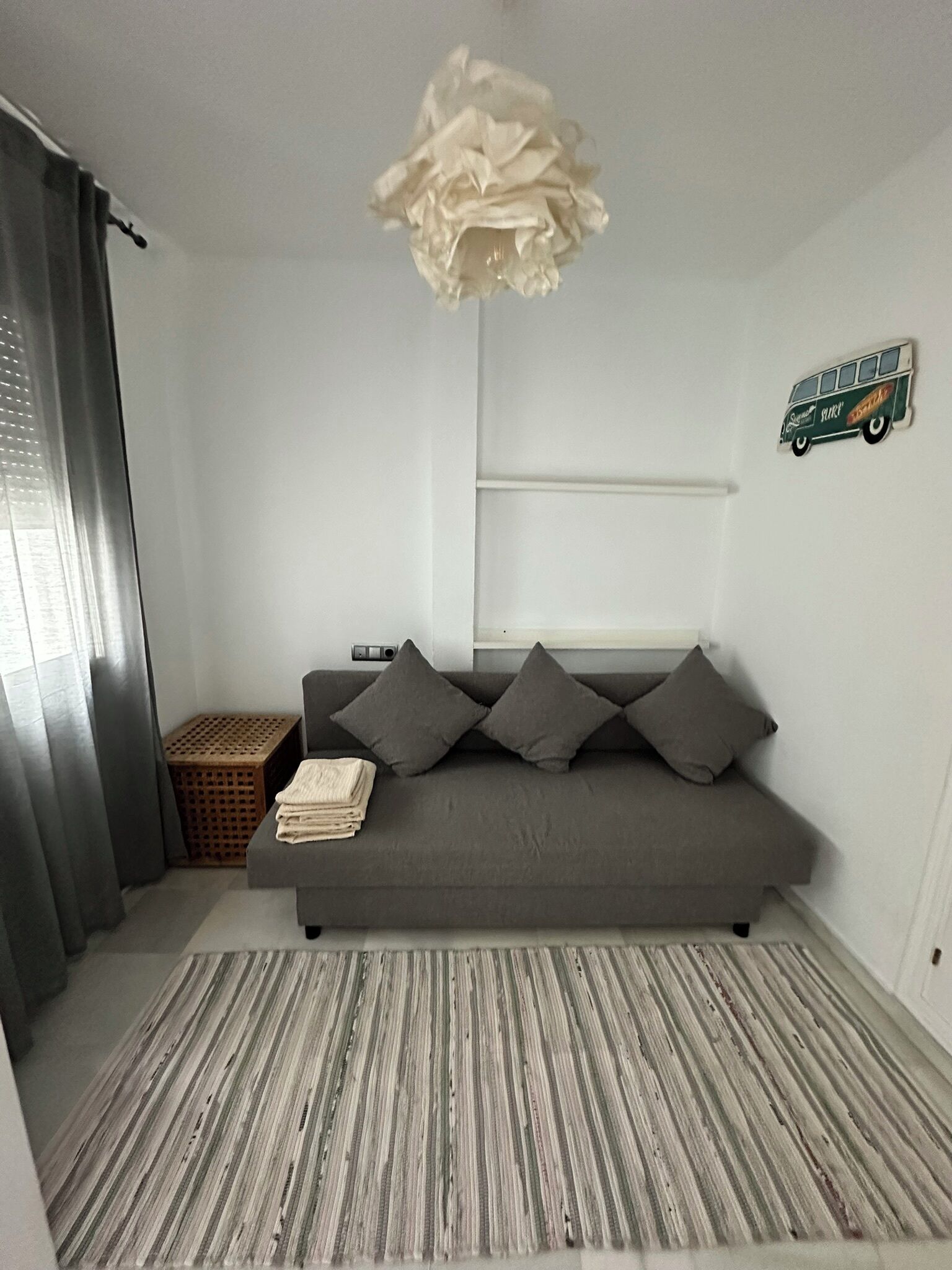 Un salon moderne avec un canapé gris, un tapis à rayures, un luminaire suspendu et un élément décoratif fixé au mur.