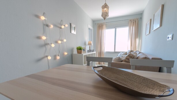 Un soggiorno moderno con un tavolo da pranzo in legno, una ciotola decorativa, luci a stringa e un divano.