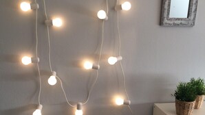 Una parete con una fila di lucine bianche e una piccola pianta in vaso su uno scaffale bianco.