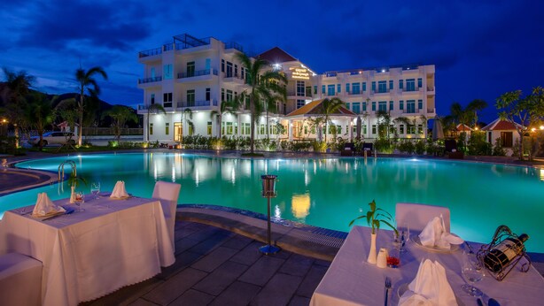 Un hotel con piscina, zona de comedor al aire libre y fachada iluminada.