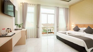 Habitación de hotel con cama, escritorio con bandeja de artículos de aseo, televisor montado en la pared y balcón con cortinas.