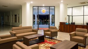 Un hall de hotel con mostrador de recepción, sofás y suelo alfombrado.