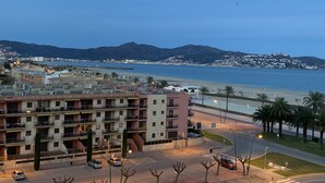 A coastal cityscape with a prominent hotel building featuring multiple floors and balconies, a beachfront, and distant mountains. -  Apartment 1st Line Beach-WIFI-A / A (Empuriabrava)