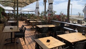An outdoor patio with wooden tables and chairs, umbrellas, and plants. -  Apartment 1st Line Beach-WIFI-A / A (Empuriabrava)