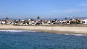 A coastal town with a sandy beach and ocean. There are buildings with balconies and palm trees. -  Apartment 1st Line Beach-WIFI-A / A (Empuriabrava)