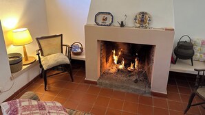 Una sala de estar con chimenea, una silla de mimbre, una mesa con lámpara y un cuadro en la pared.