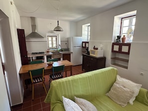 Una cocina compacta con comedor, un sofá verde y un ventanal con vistas.