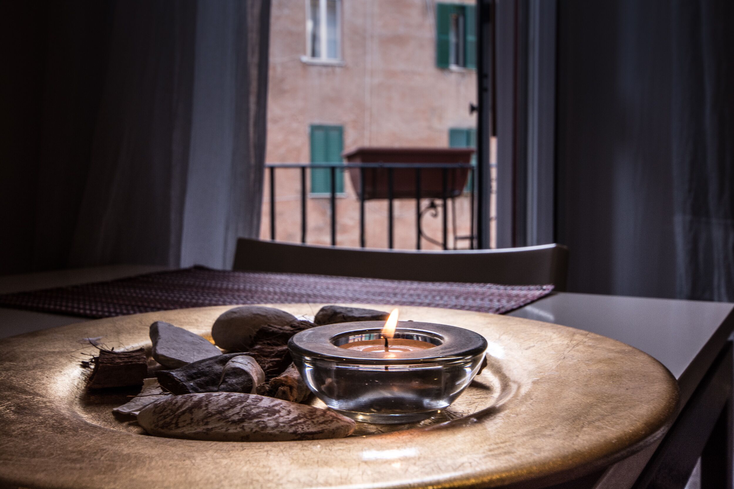 A round wooden table with a candle in a glass holder, surrounded by stones and a woven placemat.