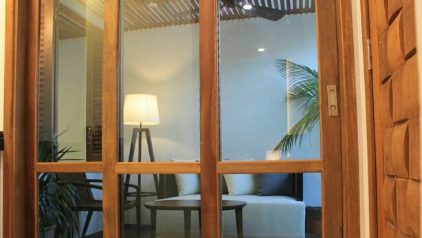 A room with a sliding glass door leading to an outdoor seating area with a sofa, two chairs, a table, and a lamp. - Sandy Garden Resort (Langkawi)