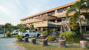 A multi-story building with a parking area, palm trees, and a rock garden. - Sandy Garden Resort (Langkawi)