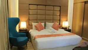 A hotel room with a large bed, two bedside tables with lamps, a blue armchair, and a wooden wardrobe. - Sandy Garden Resort (Langkawi)