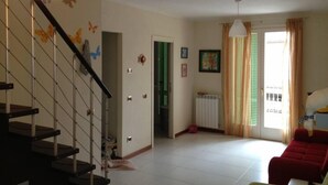 A living room with a staircase, a red sofa, a radiator, and a window with curtains. - Apartment/ flat - Marina di Massa (Marina di Massa)