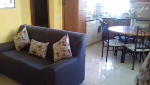 A living room with a sofa and floral cushions, a dining area with a table and chairs, and a washing machine in the background. - HOUSE "SAN MIGUEL" Entire apartment "<br>Free WIFI (Morro Jable)