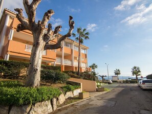 Un edificio de varios pisos con balcones, una palmera y un coche estacionado en la calle.