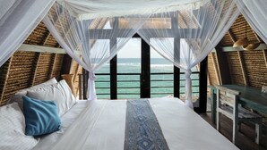 Un dormitorio con una cama grande, ropa de cama blanca, una almohada azul y vista al mar desde un balcón.