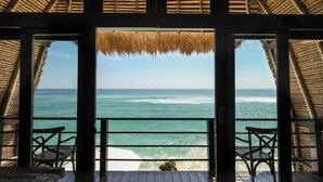 Una terraza de madera con techo de paja, con vista al océano. Hay dos sillas de madera y una mesa.