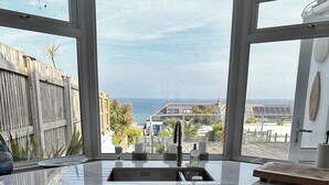 Une cuisine dotée d’une grande fenêtre donnant sur la côte, avec un évier, des placards et un plan de travail.