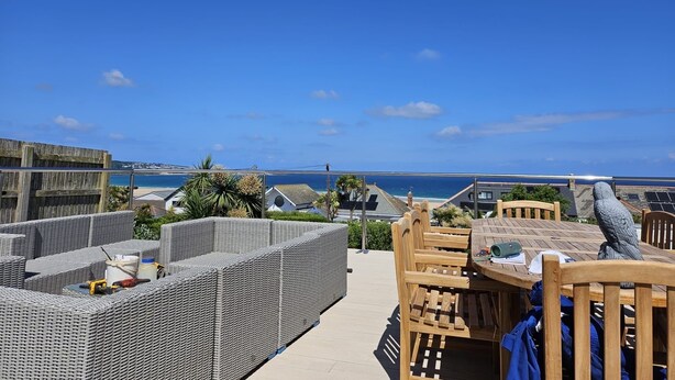 Une terrasse sur le toit, aménagée avec des meubles en osier, une table en bois et offrant une vue sur l’océan.